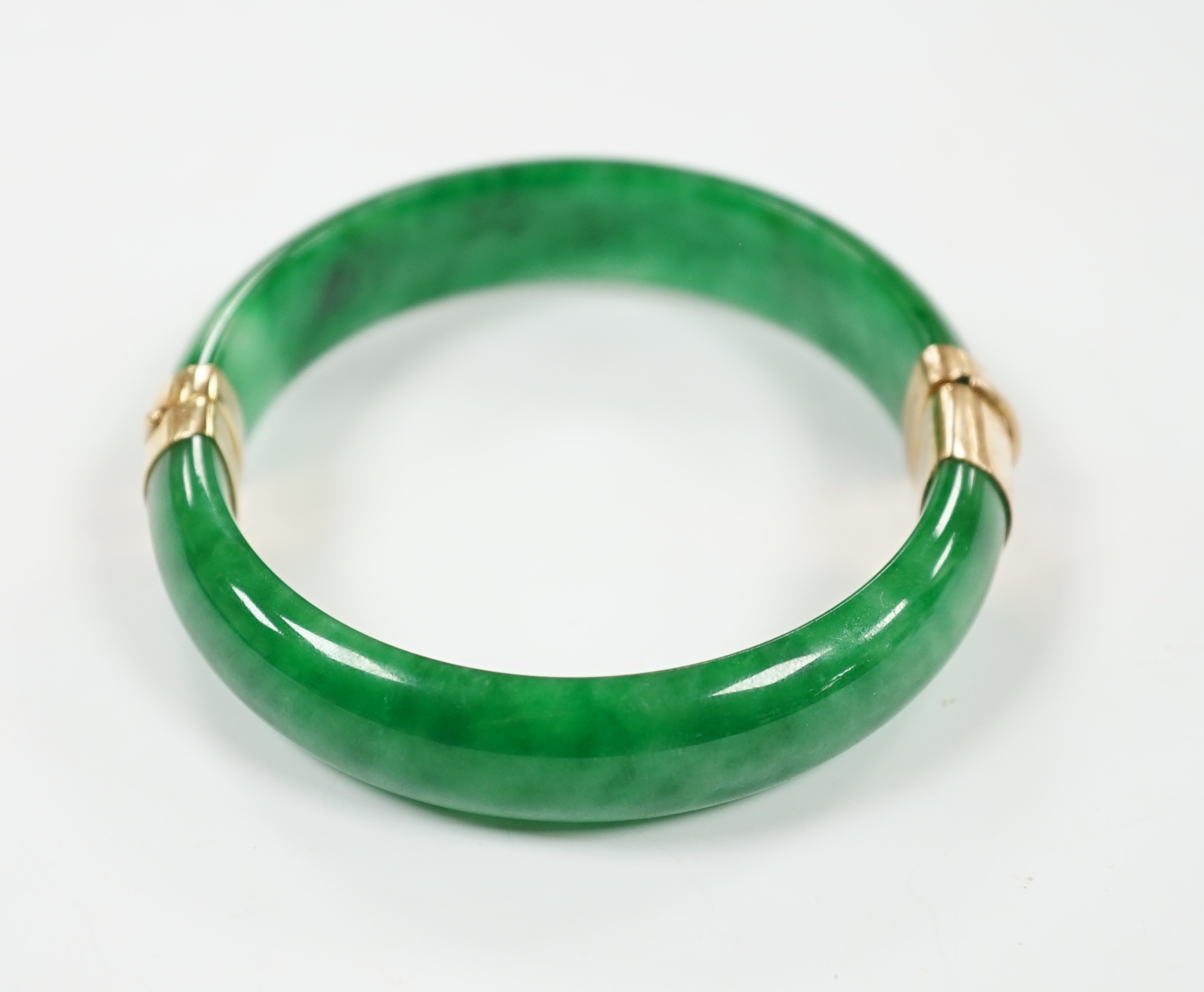 A yellow metal mounted jadeite hinged bangle, interior diameter 58mm, gross weight 59 grams.